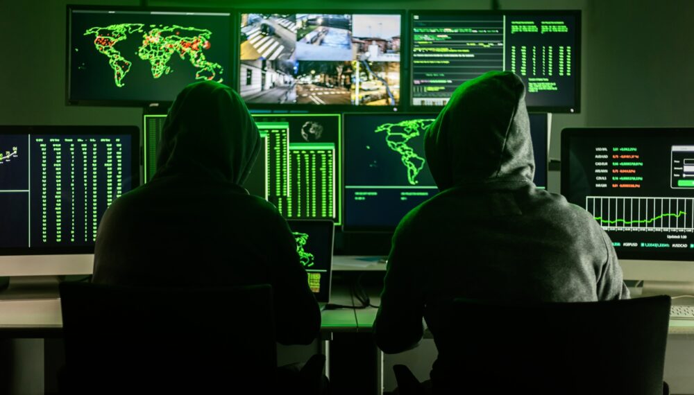 Hackers working on computers showing world maps and security camera footage Hackers working on computers showing world maps and security camera footage